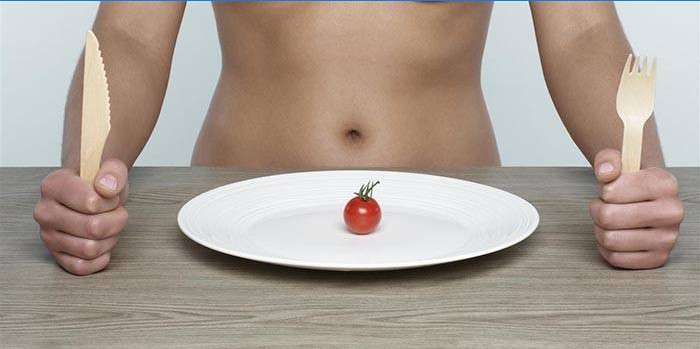 Flicka vid bordet och en liten tomat på en platta