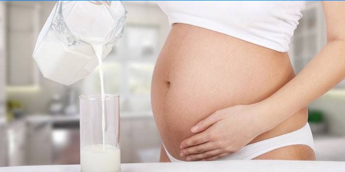 Gravid kvinna häller jäsad bakad mjölk i ett exponeringsglas