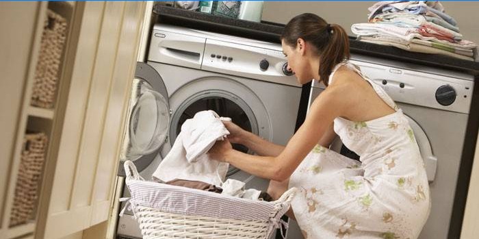 Flickan sätter handdukar i en tvättmaskin