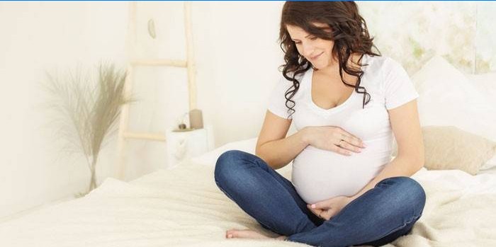 Gravid kvinna som sitter på sängen