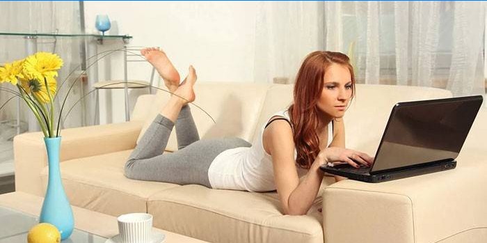 Flickan ligger på en soffa med en bärbar dator