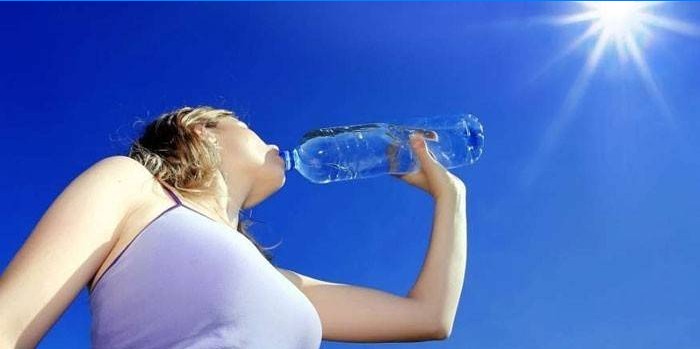 Flickan dricker vatten från en flaska